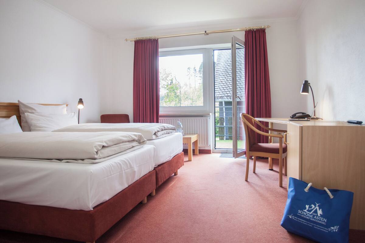 A hotel room with a bed, desk, chair, and a view of the outdoors.