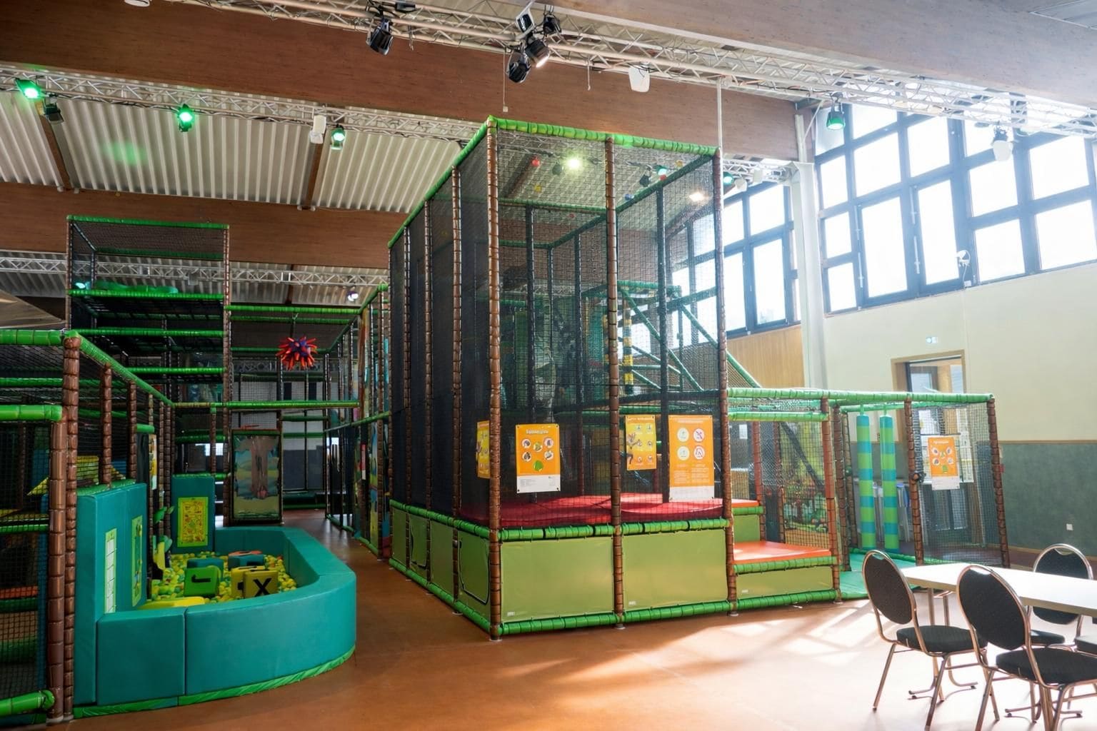 Un área de juegos interior con una estructura de escalada, toboganes y una zona de estar con mesas y sillas.