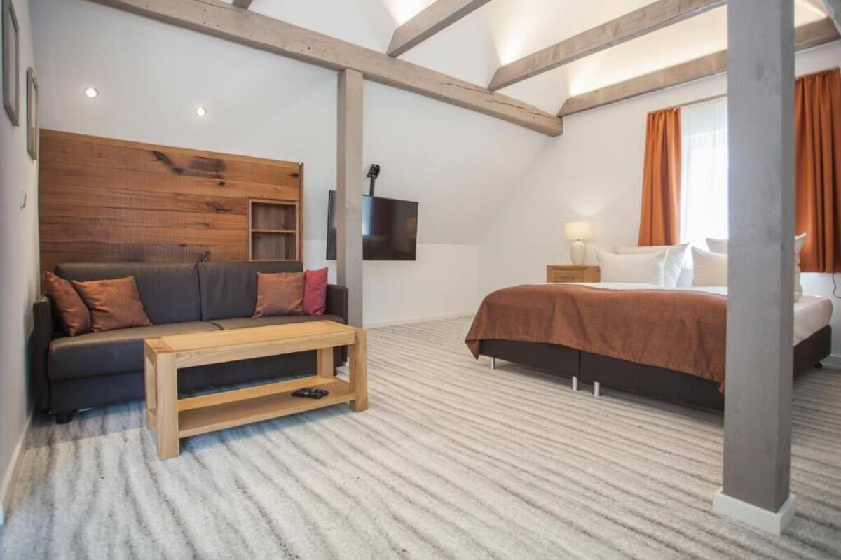 A bedroom with a bed, a sofa, a wooden headboard, a TV, and a window with curtains.