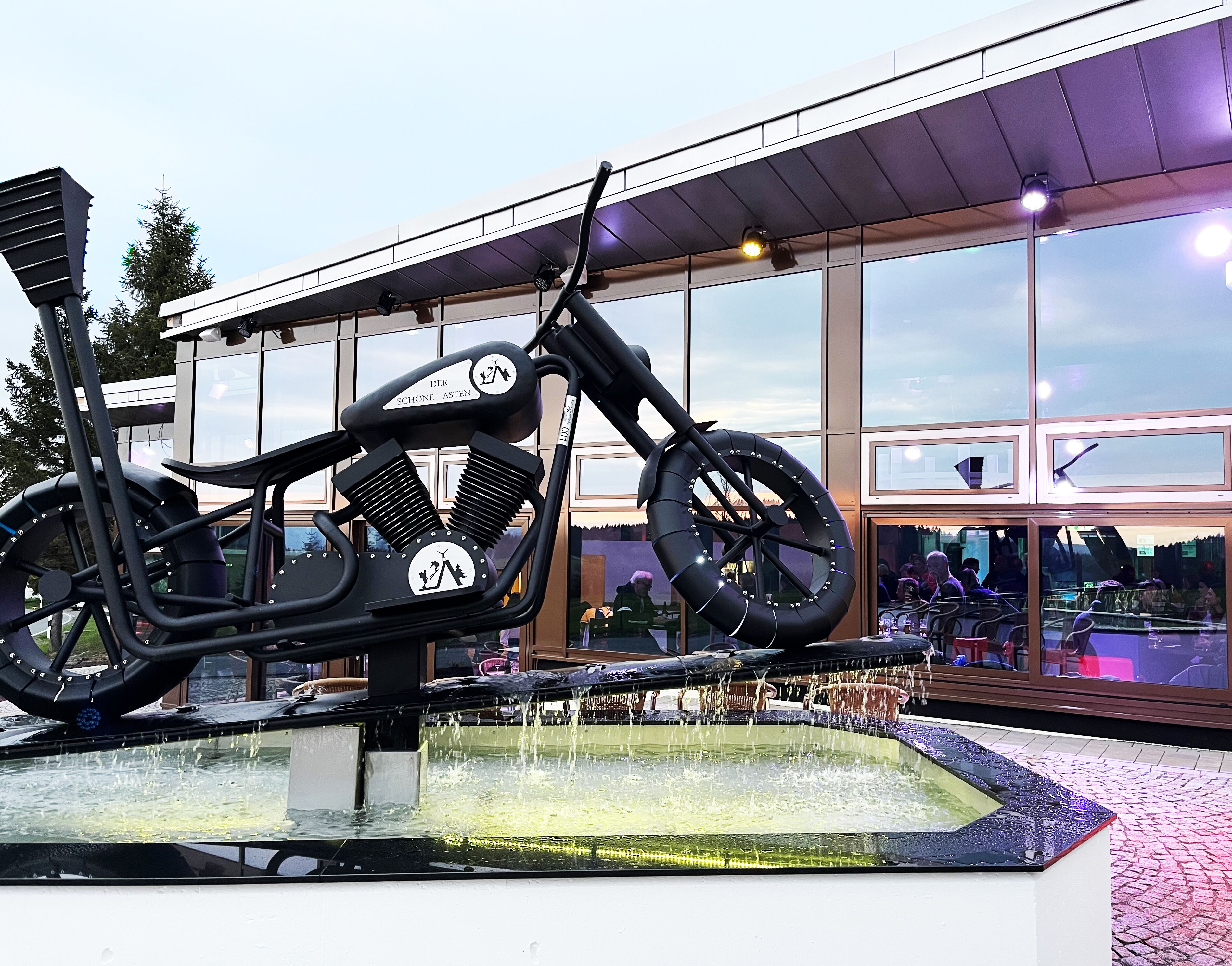 A motorcycle sculpture in front of a building with large windows.