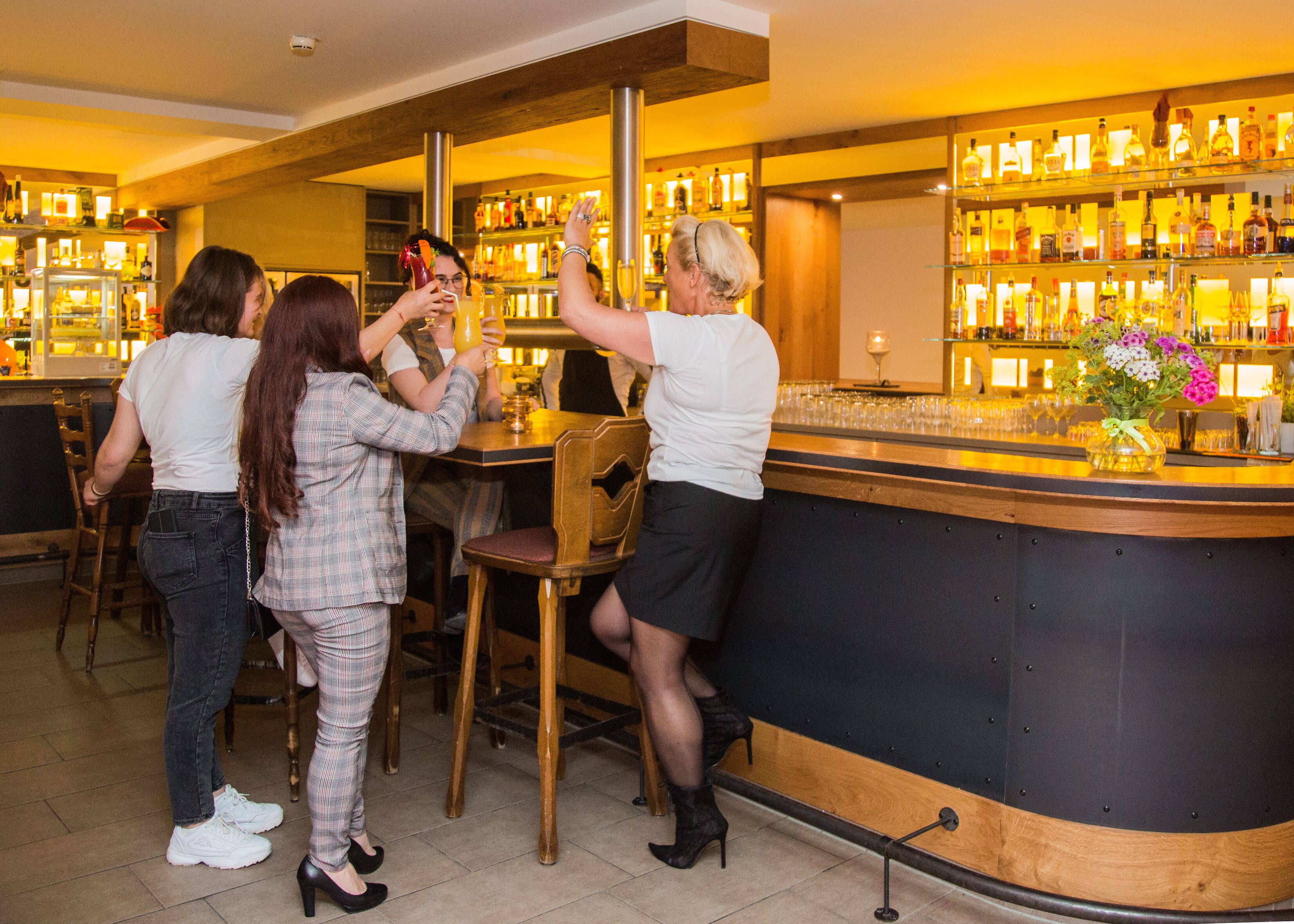 A bar area with a counter, chairs, and a variety of bottles and glasses.