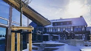 Un espace extérieur enneigé avec une structure en bois, un bâtiment doté de grandes fenêtres et un toit recouvert de neige.
