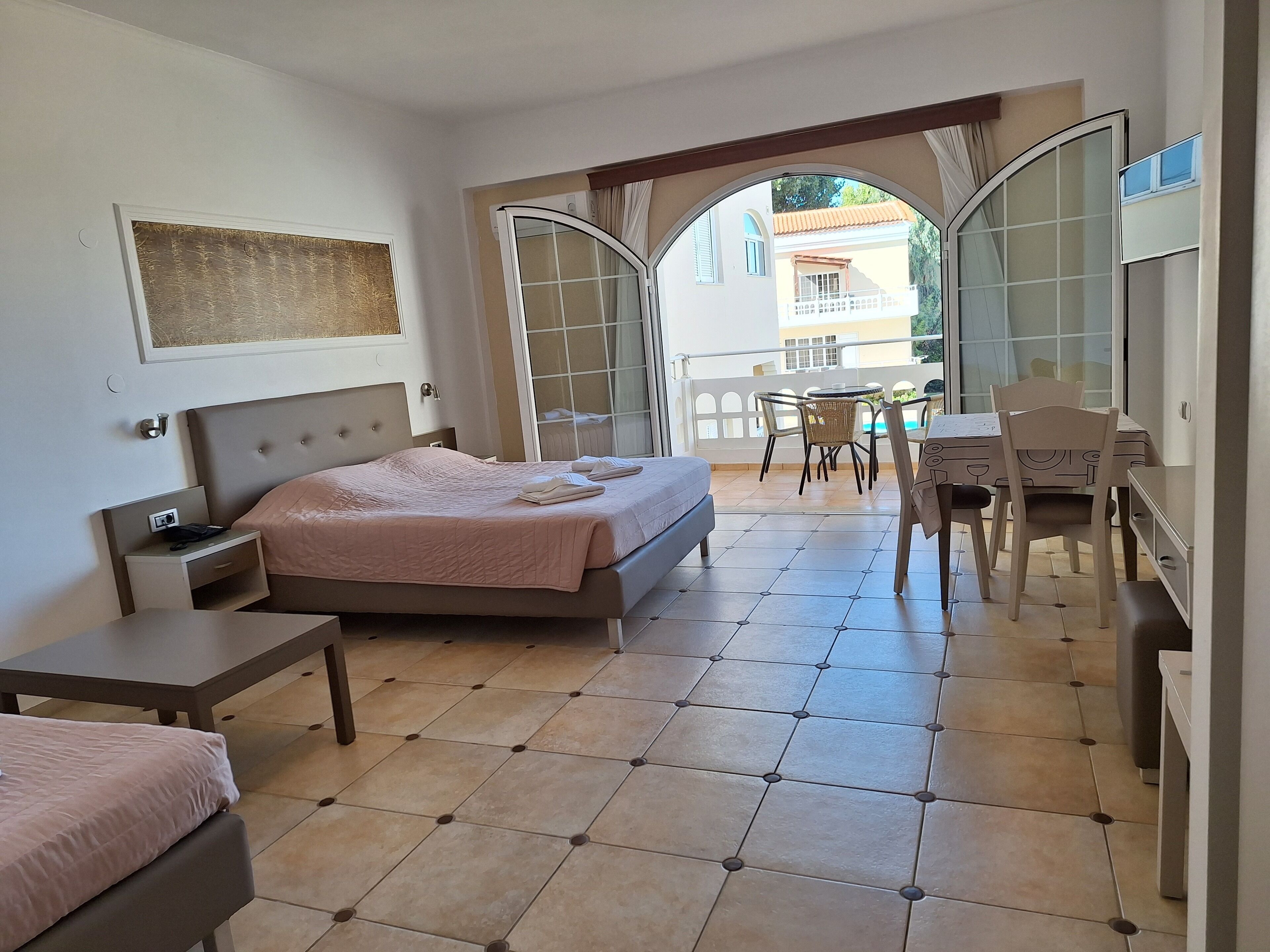 A hotel room with a bed, a desk, a chair, and a balcony with a table and chairs.