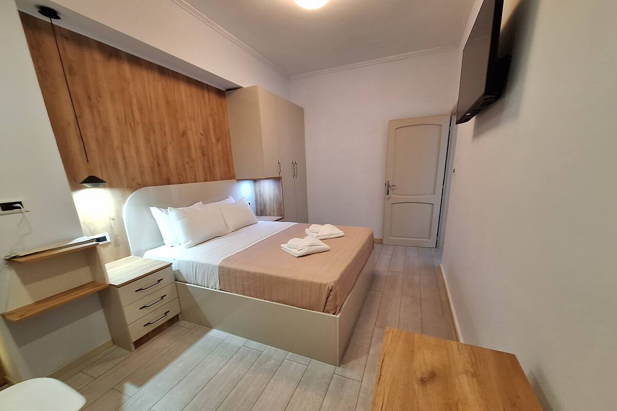 A small, neatly arranged bedroom with a bed, bedside table, and a TV mounted on the wall.