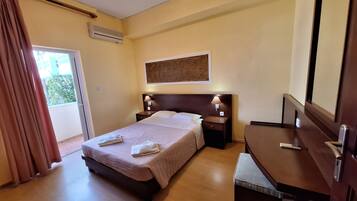 Een hotelkamer met een bed, nachtkastjes, een bureau, een stoel, een raam met gordijnen en een airconditioning.