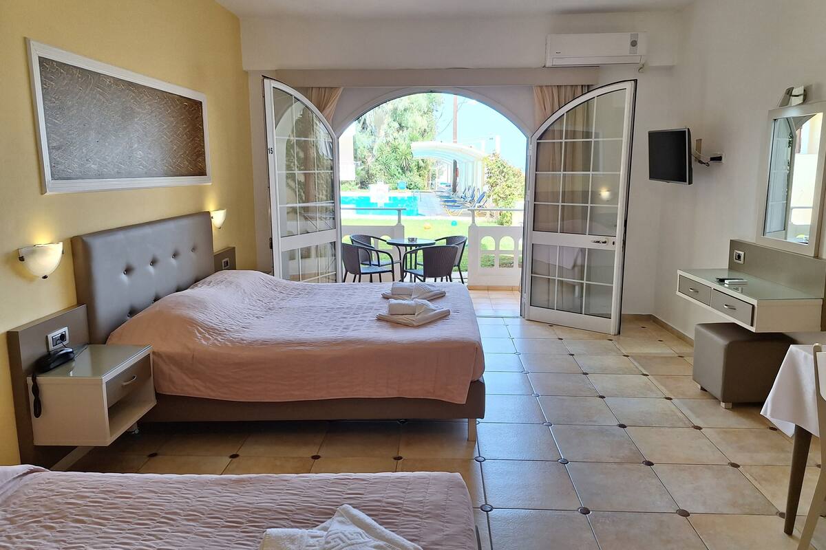 A hotel room with a large bed, a desk, a chair, and a balcony with a view of the outdoors.