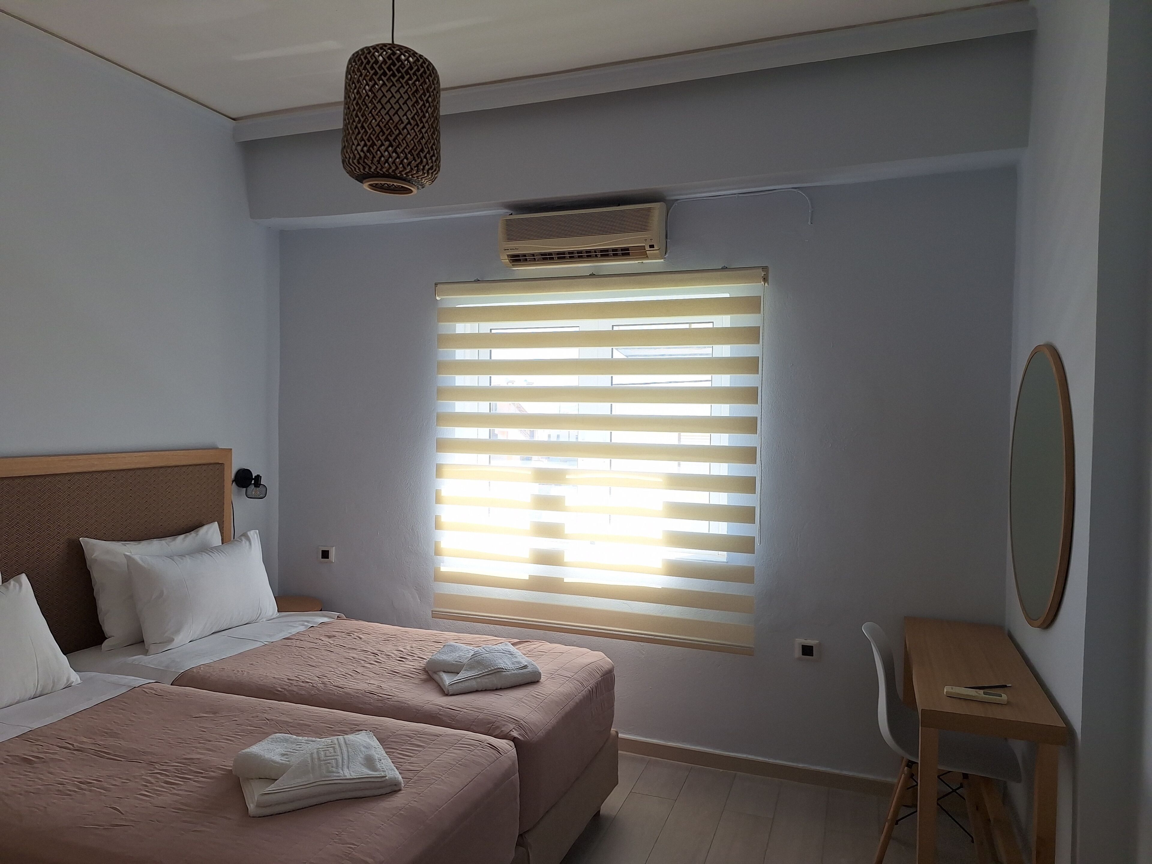 A bedroom with two beds, a desk, and a window with blinds.