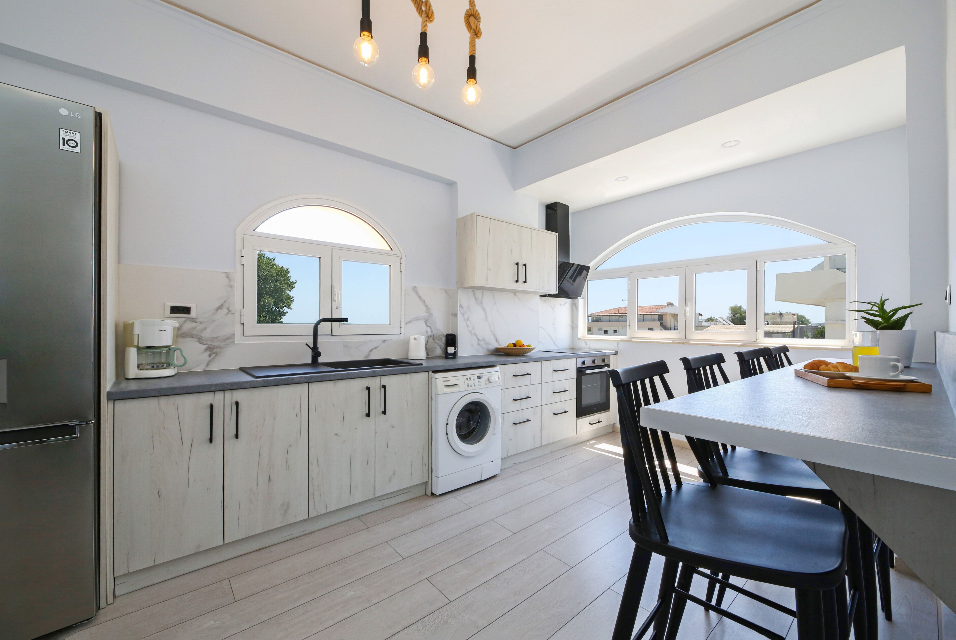 Una cocina moderna con lavadora incorporada, una zona de comedor con una mesa grande y sillas, y vistas a través de las ventanas.