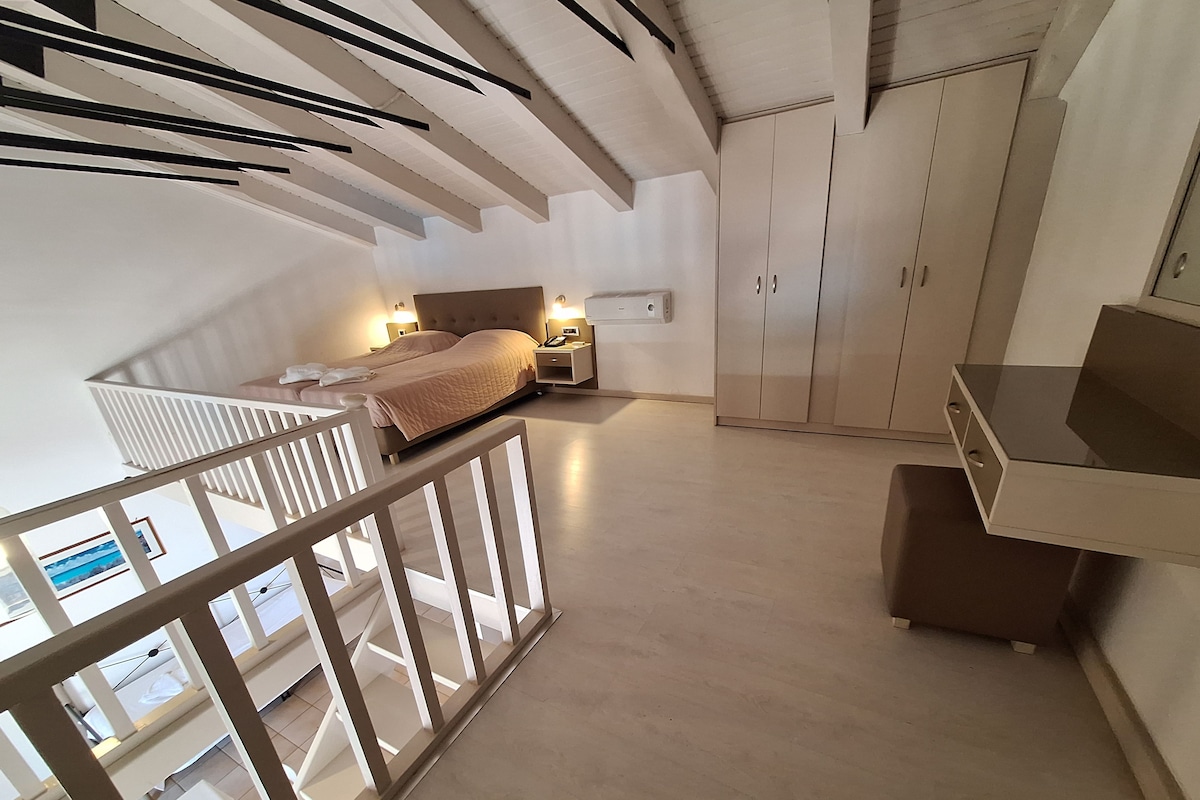 A spacious bedroom with a large bed, bedside tables, and a wardrobe. A balcony with a railing is visible.