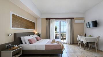 A hotel room with a bed, bedside table, TV, and a balcony with a table and chairs.