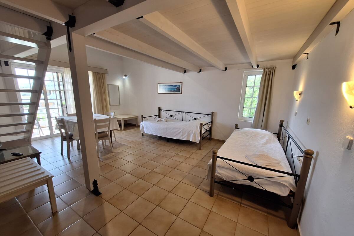 A spacious bedroom with a large bed, a smaller bed, a desk, and a chair. There is a staircase leading to another level.