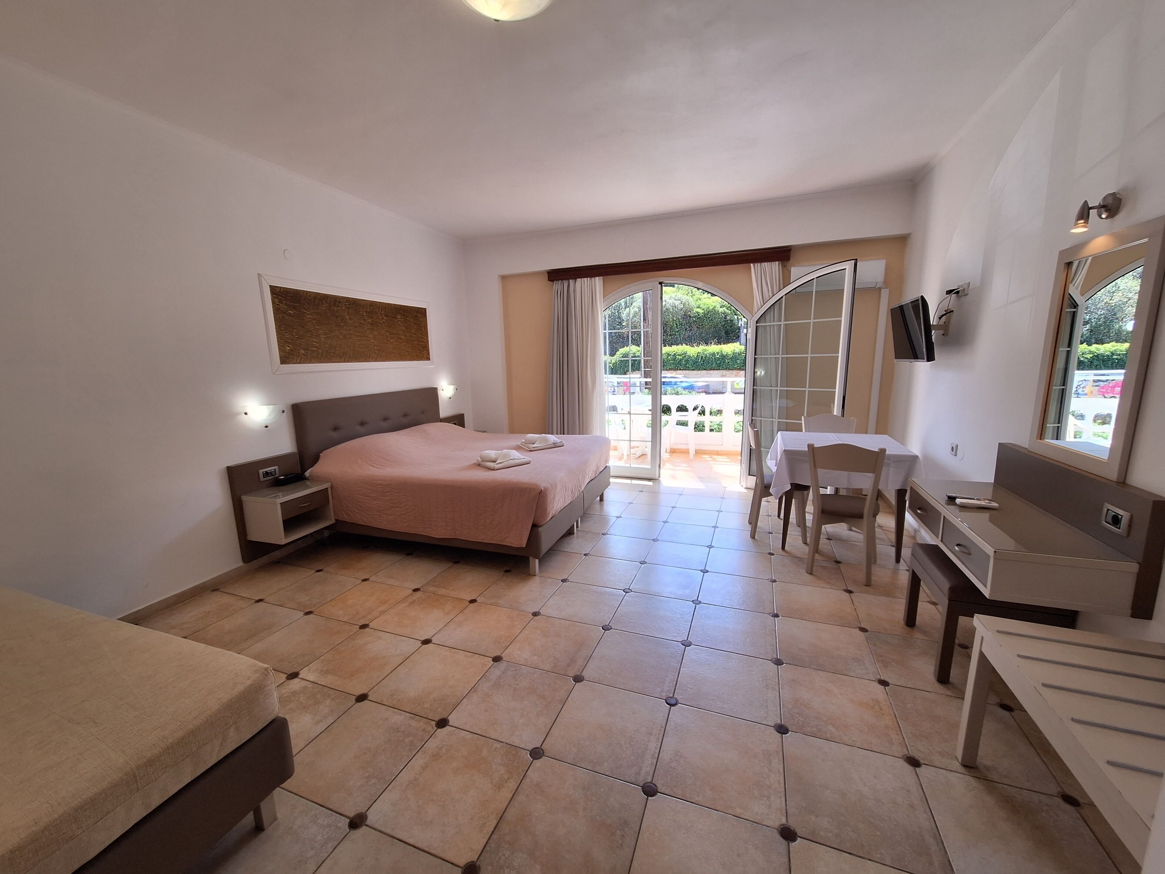 Hotelkamer met een bed, bureau, stoel, televisie en balkon met uitzicht op de omgeving.