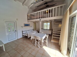 A room with a bed, a table with chairs, a staircase, and a door. - Perla Beach (Chania)
