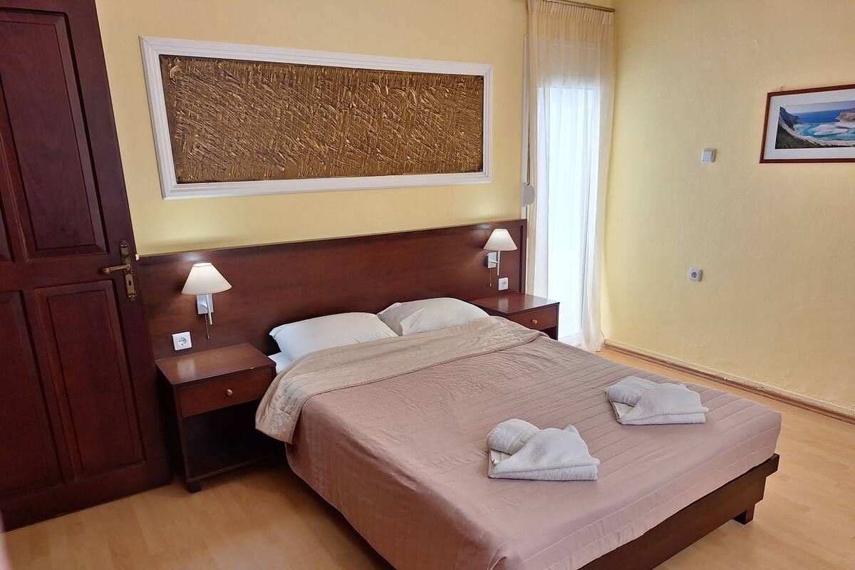 A neatly made bed with a brown headboard, two bedside tables with lamps, a large abstract painting above the bed, and a framed picture on the wall.