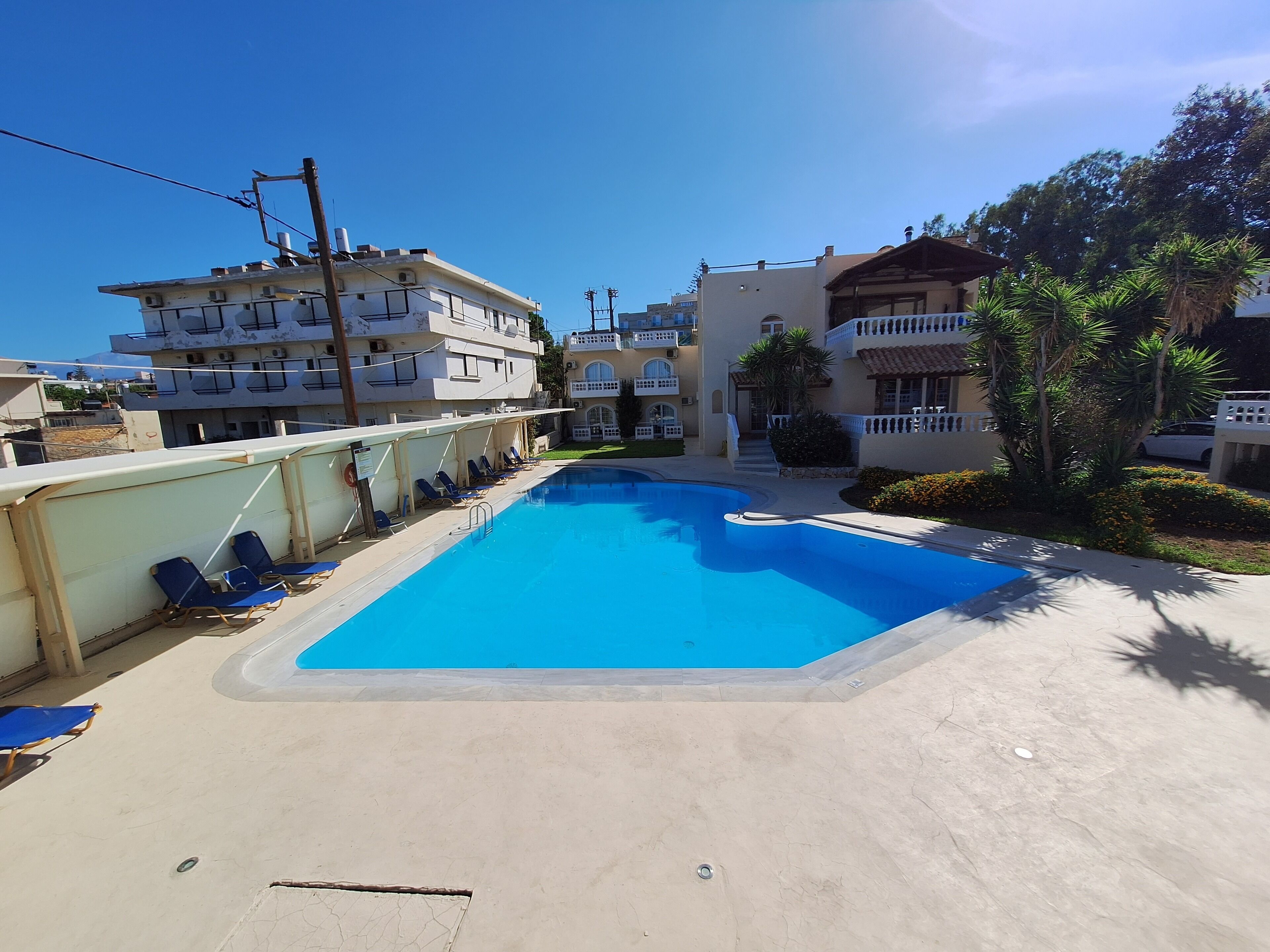 A swimming pool with blue water, surrounded by lounge chairs and a building with balconies.