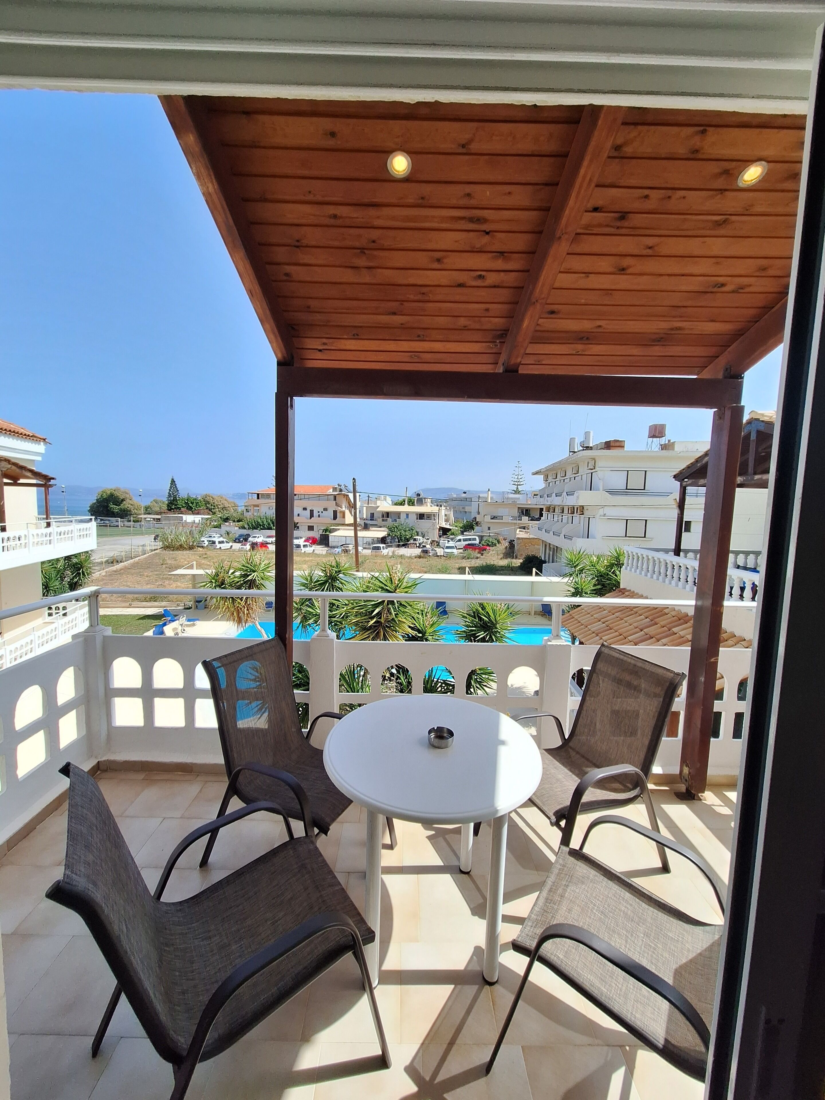 Un espacio al aire libre techado con una mesa y sillas, con vista a una piscina y edificios.