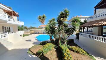 Zona de piscina con un cielo azul despejado, rodeada de edificios con balcones y una palmera.