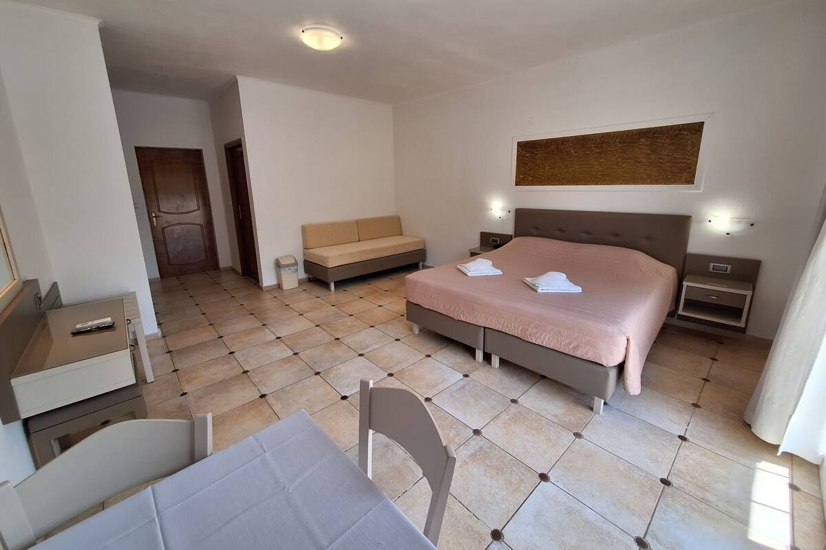 A hotel room with a bed, bedside tables, a sofa, a desk, and a chair.