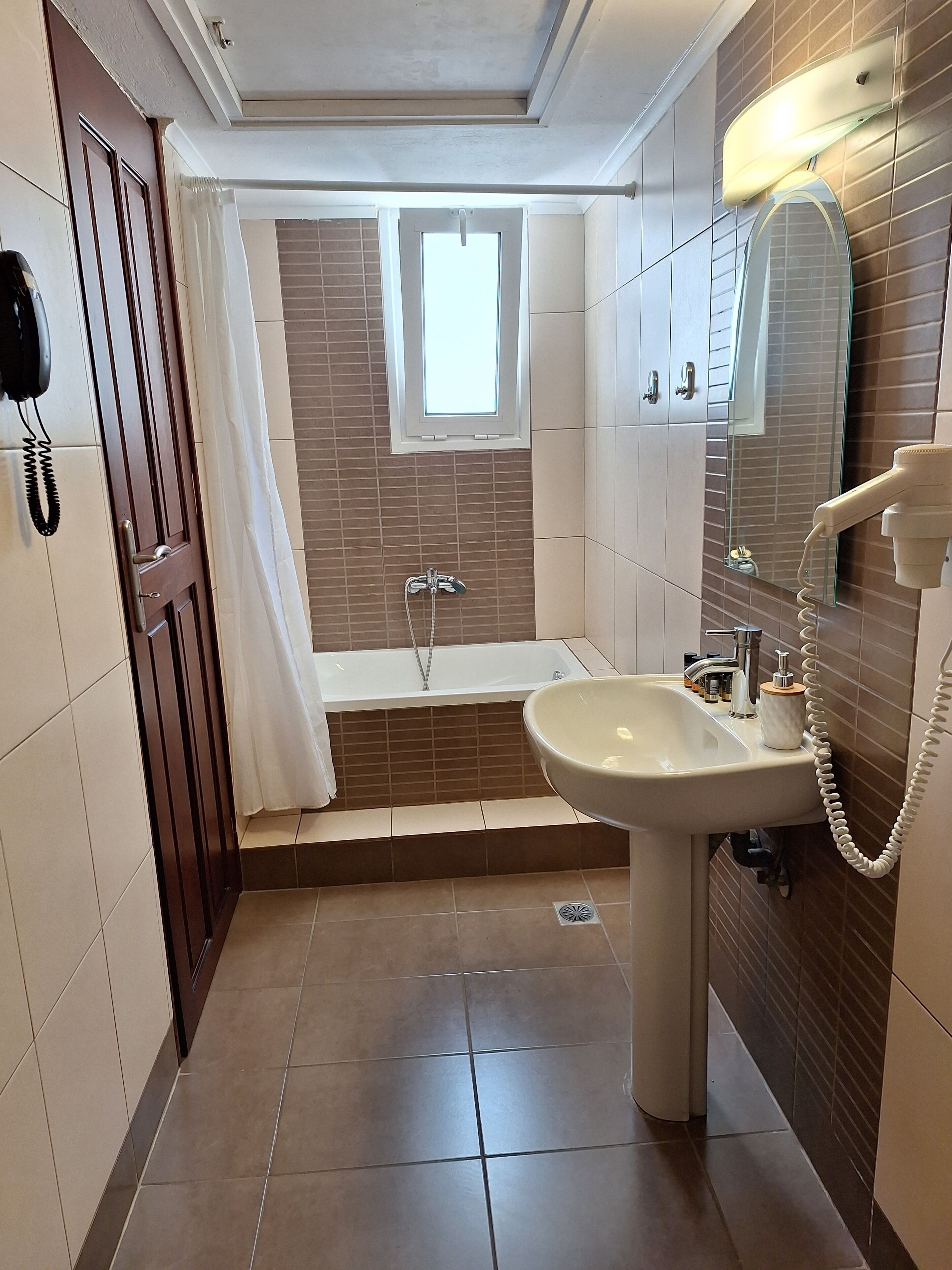 A bathroom with a bathtub, a sink, a mirror, and a telephone.