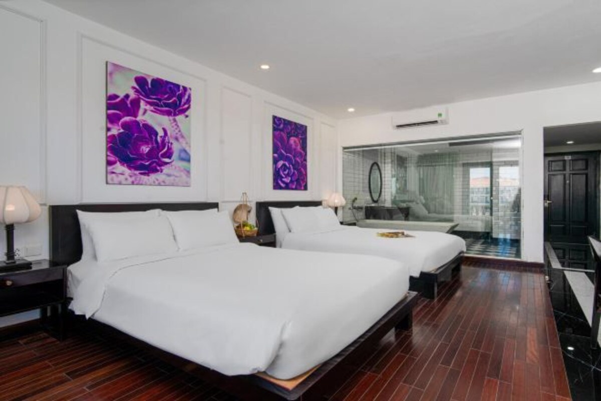 A hotel room with two beds, a large window, and artwork on the walls.