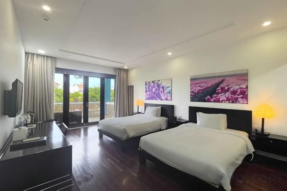 A hotel room with two beds, a desk, a TV, and a balcony with curtains.