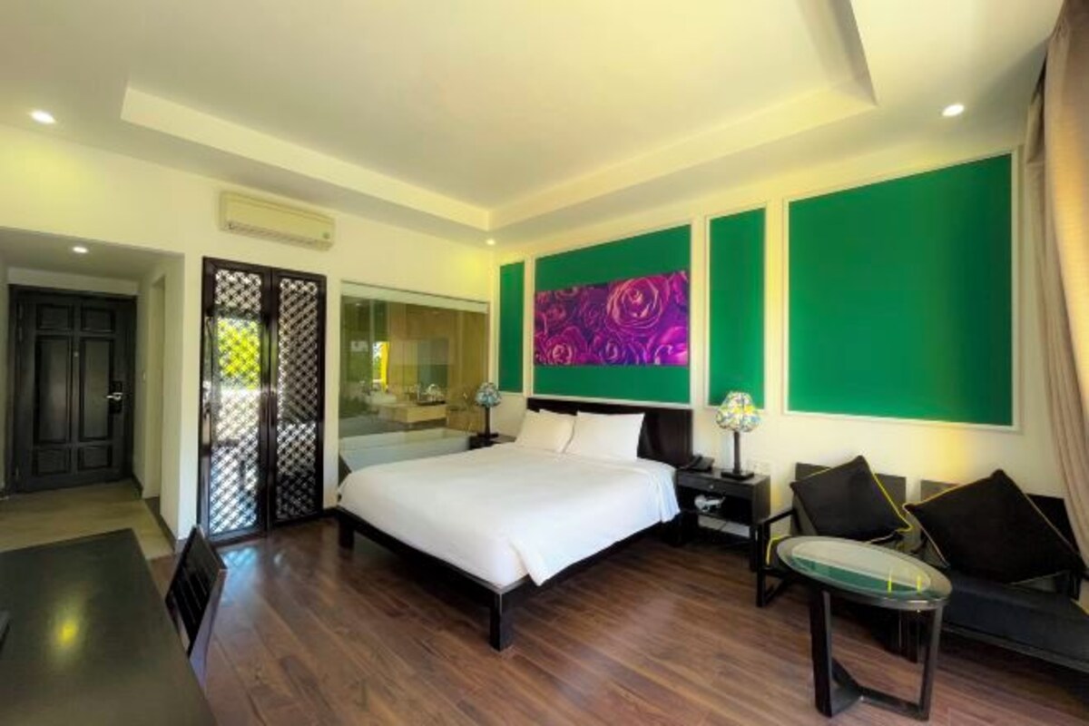 A modern hotel room with a large bed, a sitting area with a glass table, and a green accent wall.