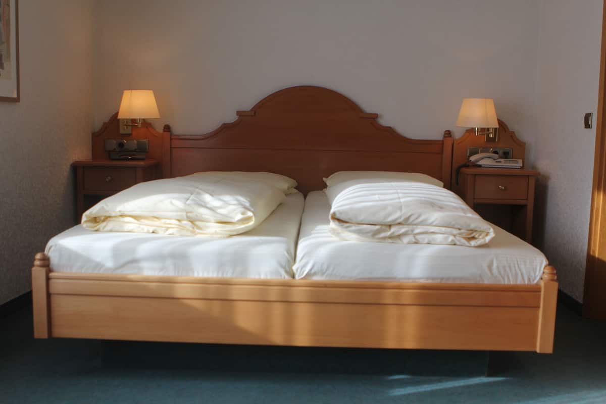 A double bed with a wooden headboard, two bedside tables with lamps, and a plain wall.