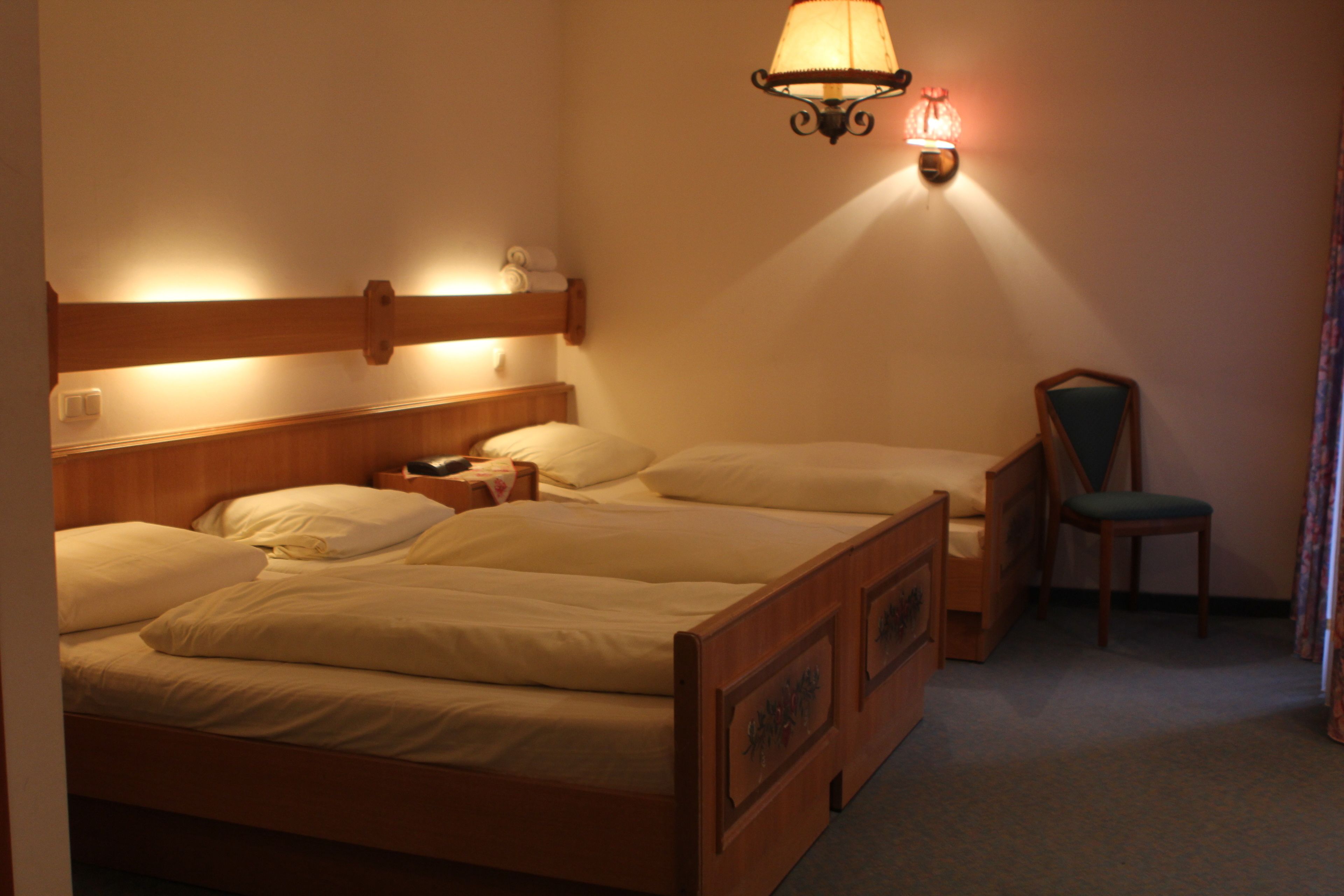 A hotel room with a large bed, a smaller bed, a chair, and a wall-mounted lamp.