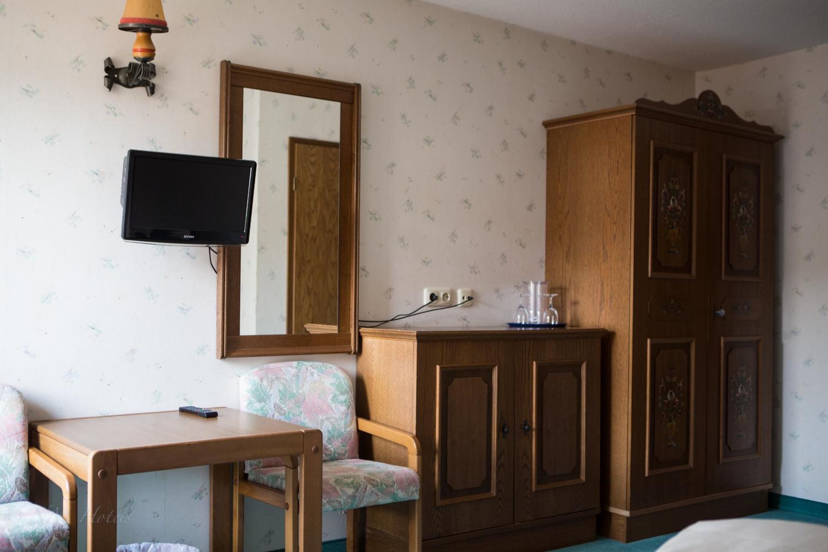 A room with a television, a mirror, a wooden cabinet, a floral chair, and a small table.