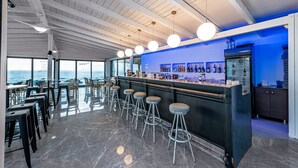Zona de bar con vista al océano, taburetes y una barra con botellas.