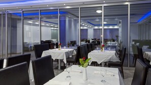 Un comedor moderno con separadores de vidrio, manteles blancos y sillas negras.