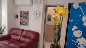 En röd lädersoffa, en orkidé i en kruka, en klocka med texten ”PARIS”, en klocka med texten ”TOKYO” och en färgstark, abstrakt målning.