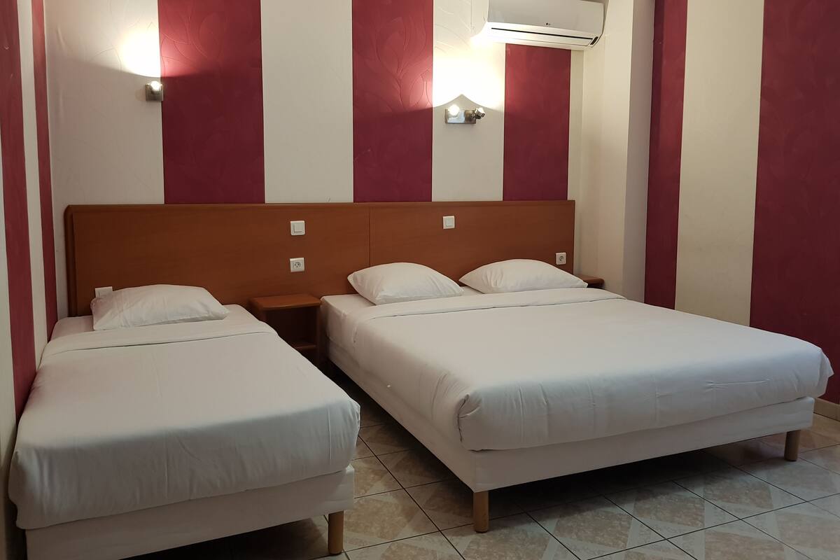 A hotel room with two single beds, a wooden headboard, a wall-mounted air conditioner, and a nightstand with a lamp.