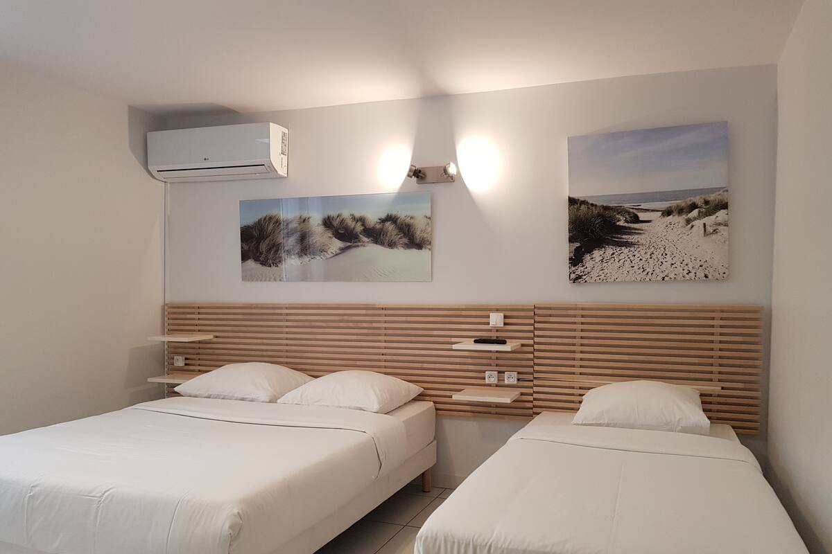 A bedroom with two beds, a wooden headboard, wall-mounted air conditioning, and two landscape paintings.