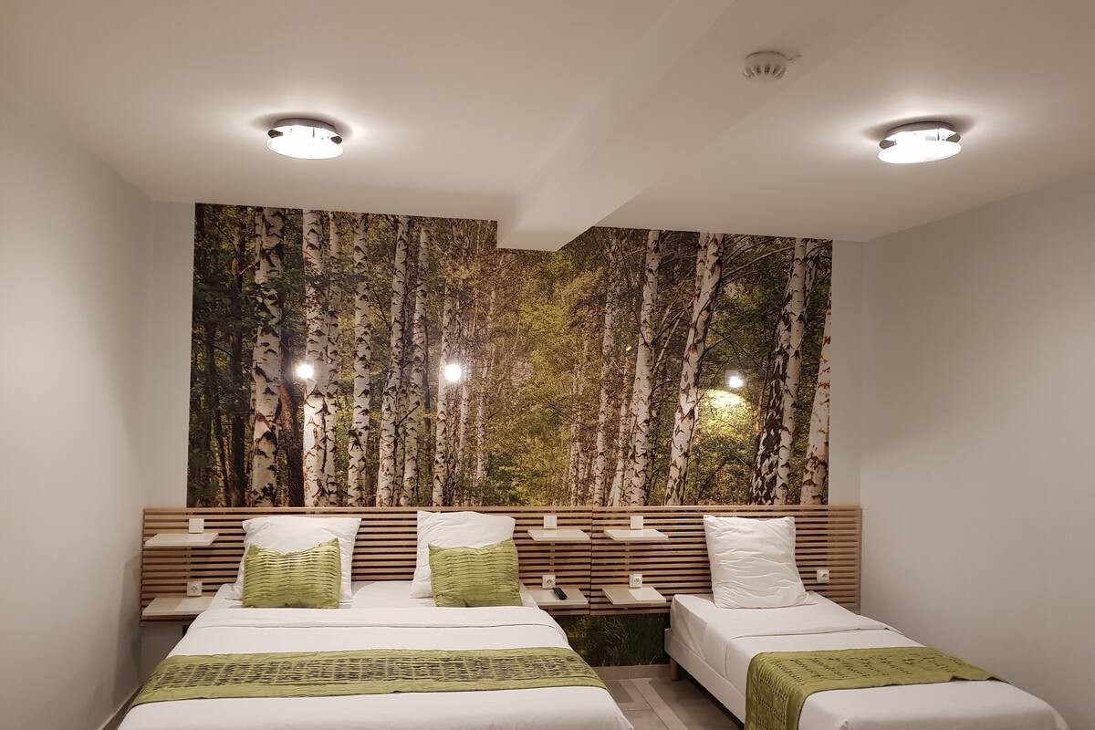 A modern hotel room with two beds, a large wall mural, and built-in nightstands.