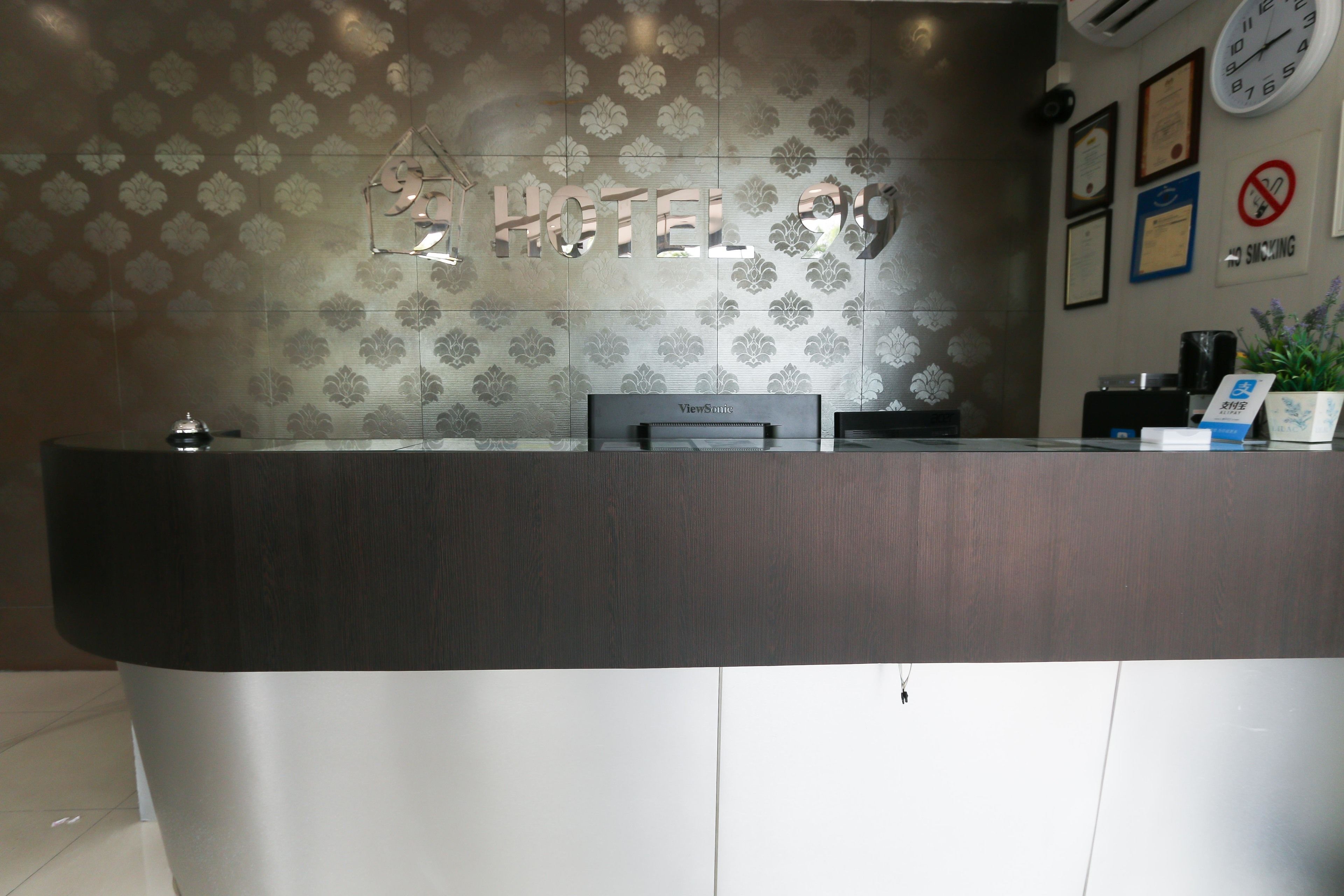 A hotel reception desk with a clock, framed certificates, and a no-smoking sign.