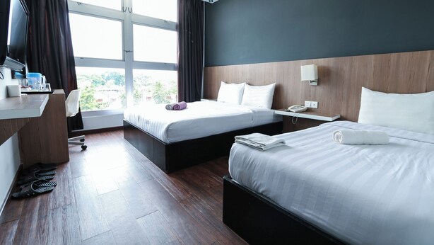 Een hotelkamer met twee bedden, een bureau, een stoel, een televisie en een raam met gordijnen.