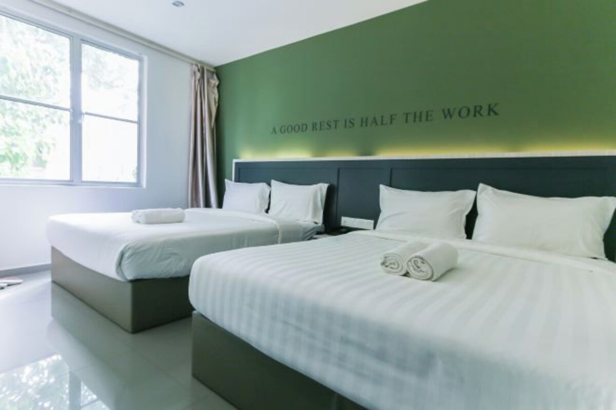 Habitación de hotel con dos camas, una pared de acento verde y una ventana con cortinas.