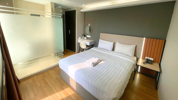 A modern hotel room with a large bed, a bedside table with a phone, a desk with a chair, a mirror, and a walk-in closet.