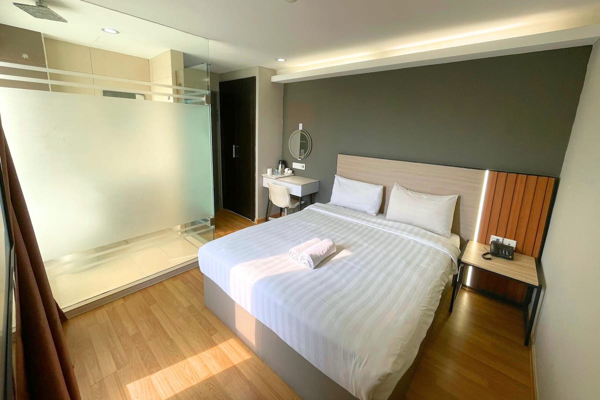 A modern hotel room with a large bed, a bedside table with a phone, a desk with a chair, a mirror, and a walk-in closet.