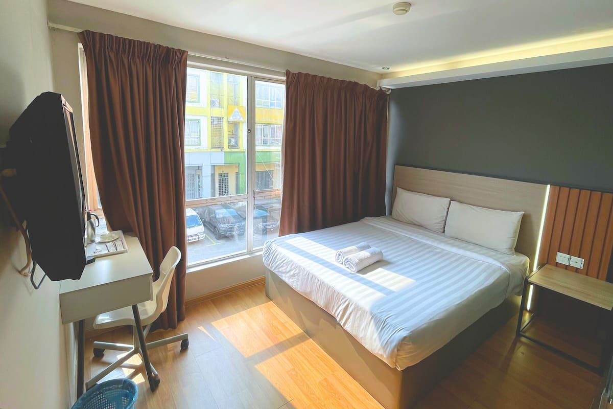A hotel room with a large bed, a desk with a chair, a TV, and a window with curtains.