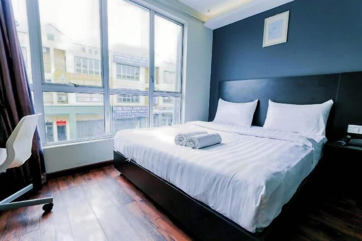A hotel room with a large window, a bed with white linens, a dark headboard, and a chair.