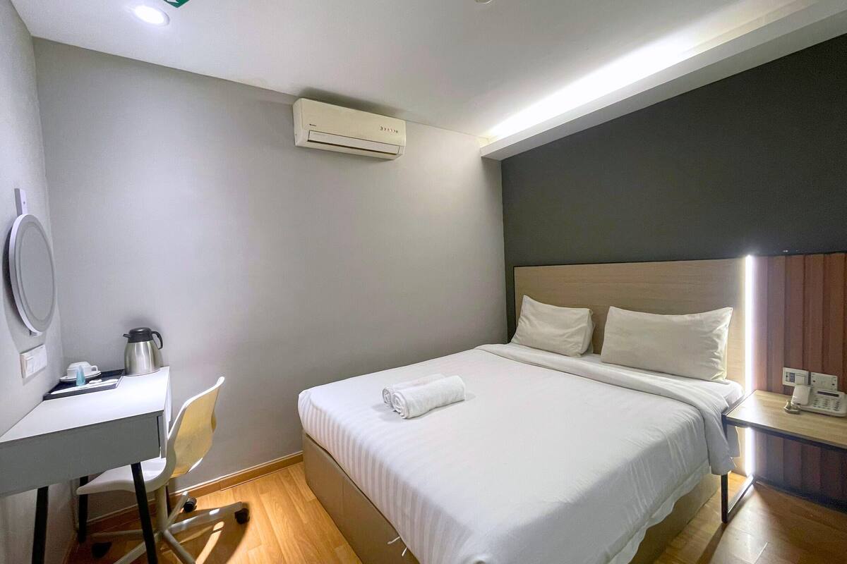 A hotel room with a bed, bedside table, and a desk with a chair.