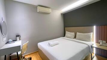 A hotel room with a bed, bedside table, and a desk with a chair.