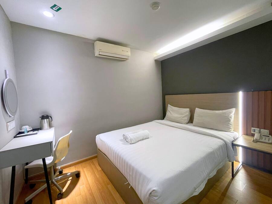 A hotel room with a bed, bedside table, and a desk with a chair.