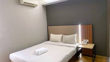 A neatly made bed with white linens and a rolled towel, a bedside table with a phone, and a wall-mounted air conditioner.