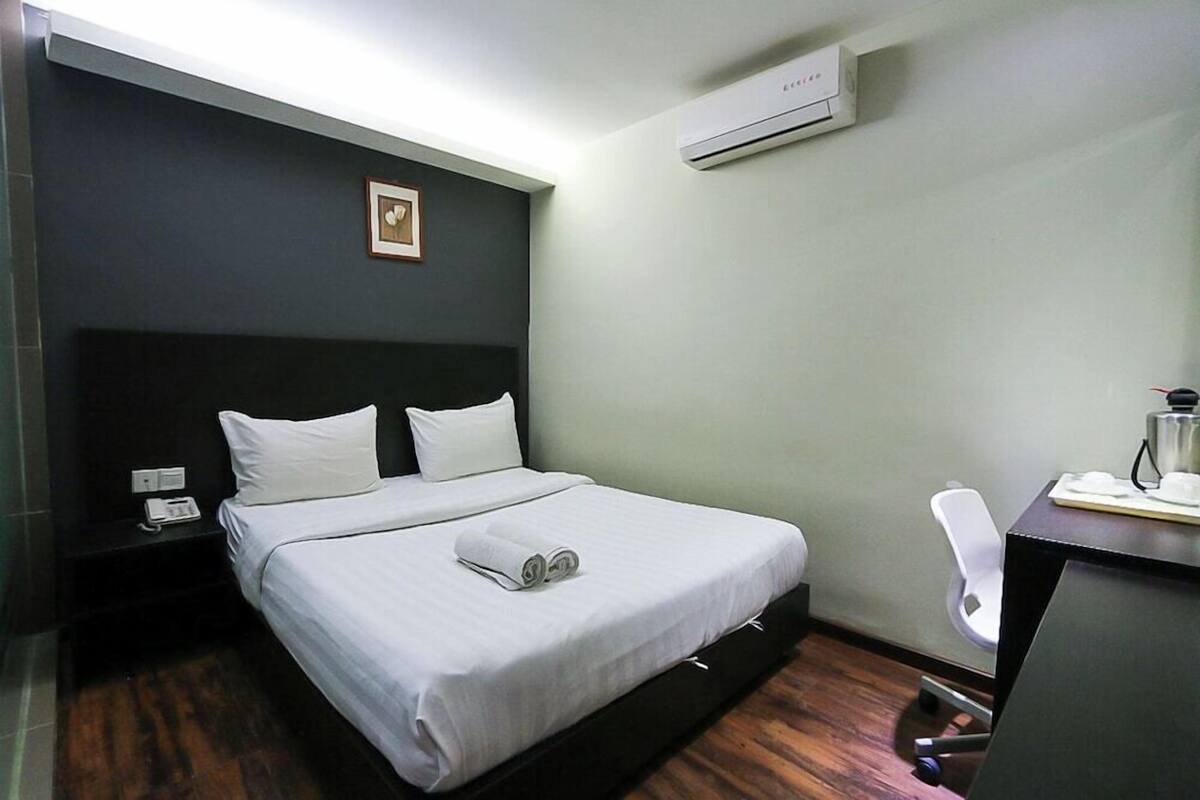 A hotel room with a bed, a desk, an air conditioner, and a chair.