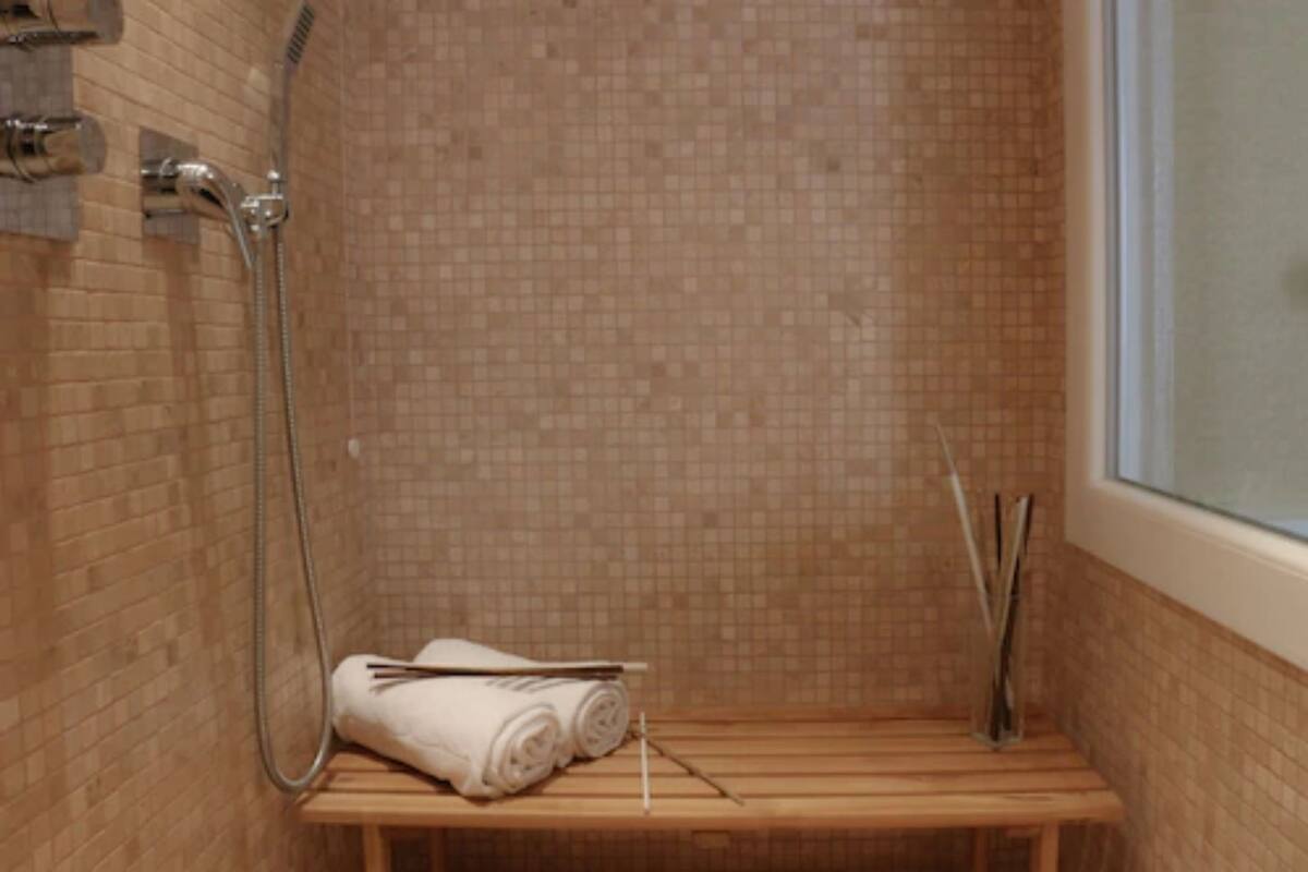 Een kleine badkamer met een douche, een houten bankje en een handdoekhouder.
