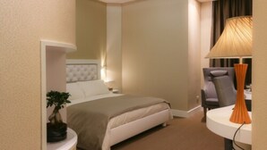 A hotel room with a bed, a bedside table with a lamp, a chair, and a small table with a lamp.