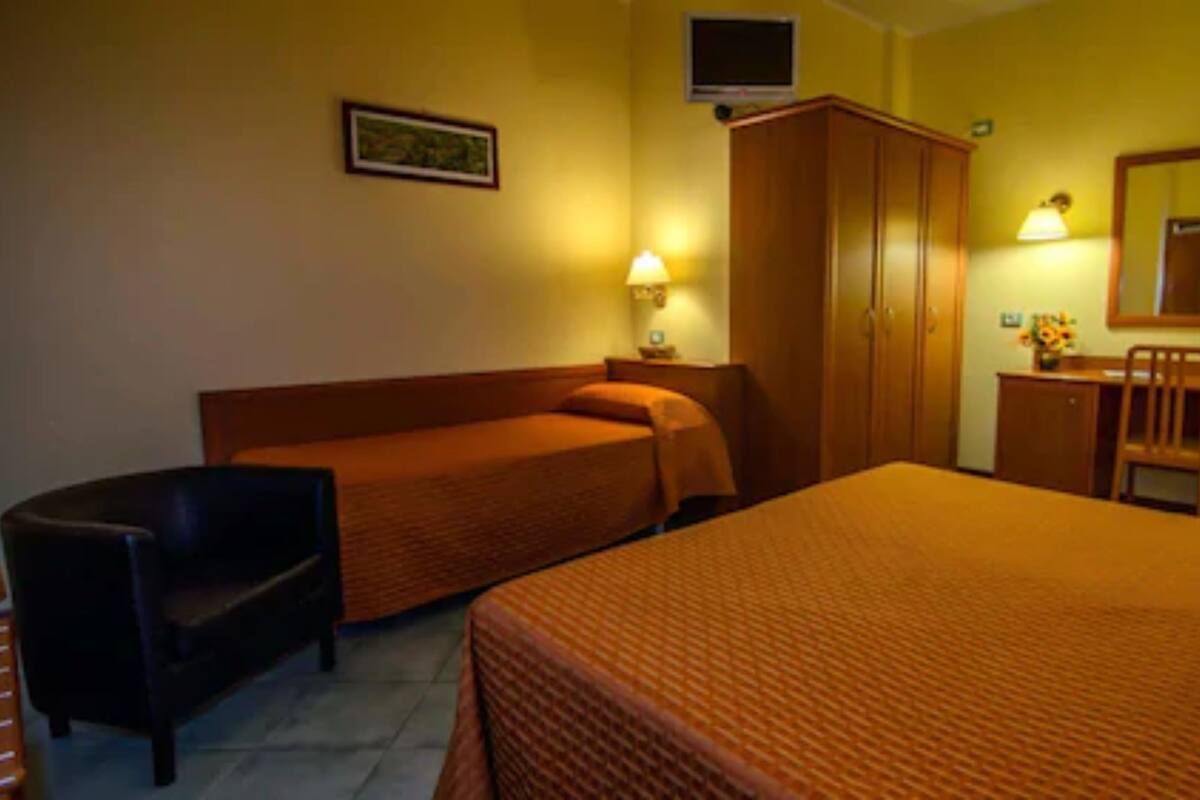 Een hotelkamer met twee enkele bedden, een bureau met stoel, een kledingkast, een televisie en een lijst aan de muur.